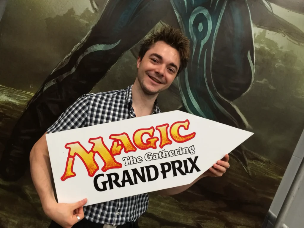 Oli hält ein Schild mit der Aufschrift Magic: The Gathering Grand Prix