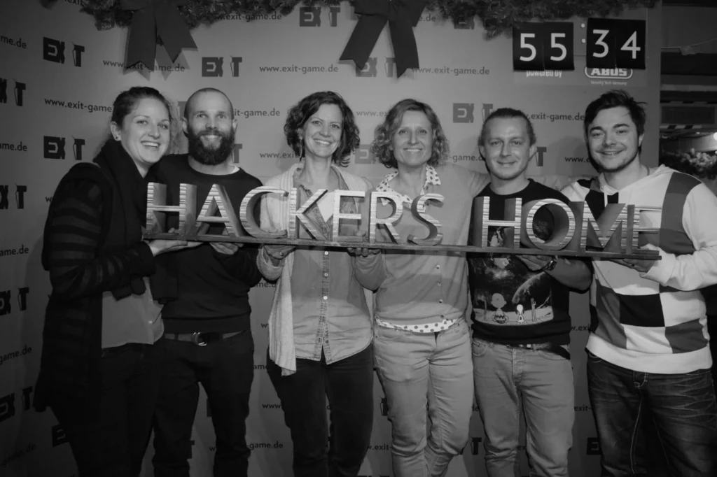 Sechs Personen halten nach einem Exit Game ein Schild mit der Aufschrift Hackers Home