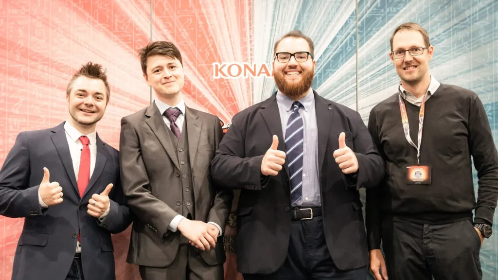 Vier Mitglieder des Coverage-Teams vor einer Konami-Wand, zwei zeigen den Daumen nach oben